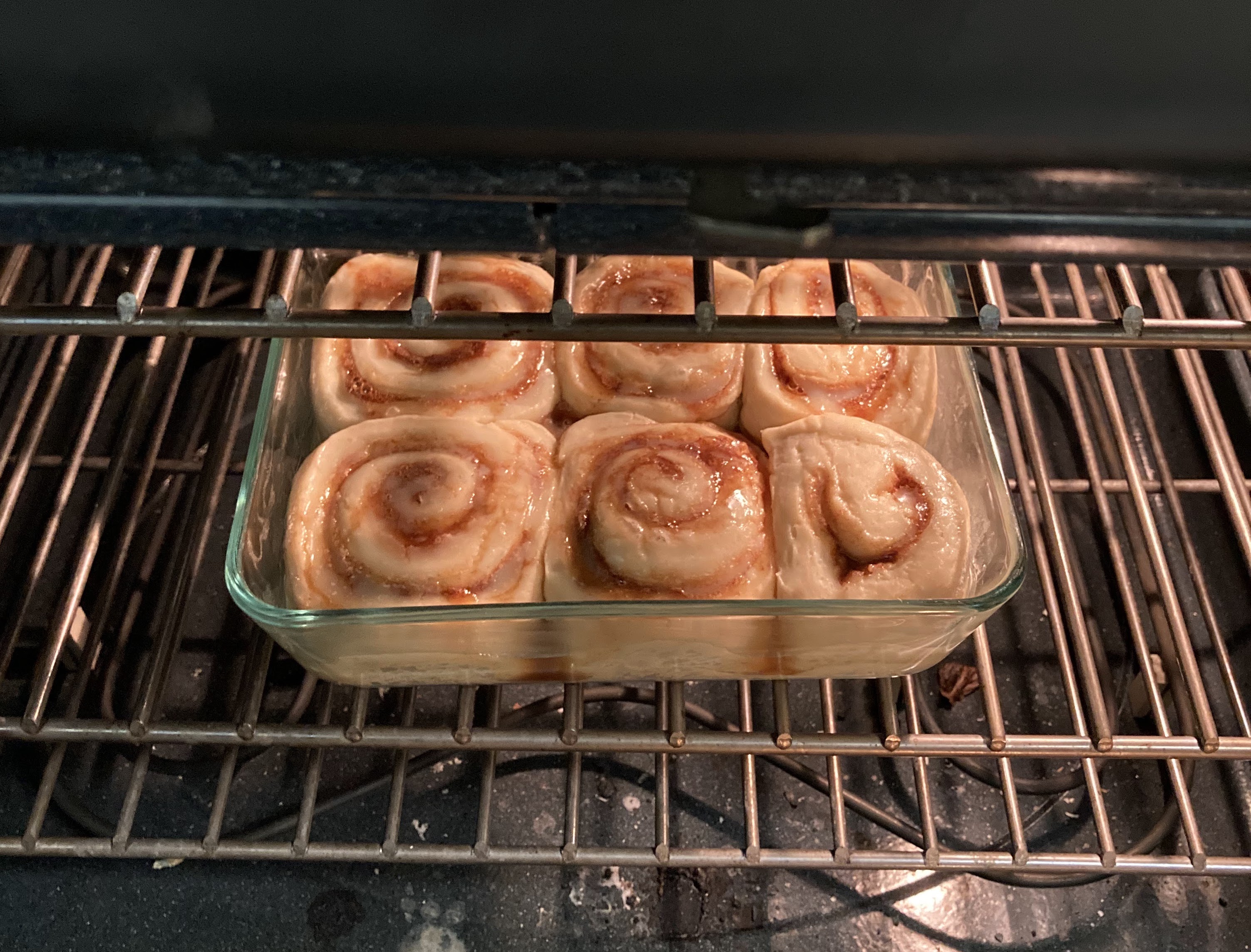 A bunch of cinnamon rolls in a baking tray in an oven.